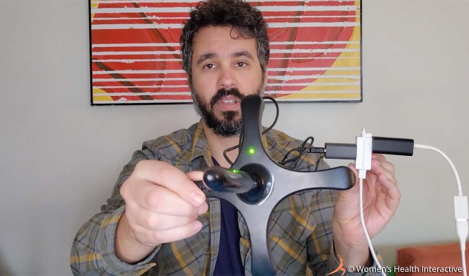 photograph of product tester justin holding the fleshlight sleeve warmer in his hand, showing it turned on and plugged in via a usb cord, its small green light on the base indicating that the warmer is on