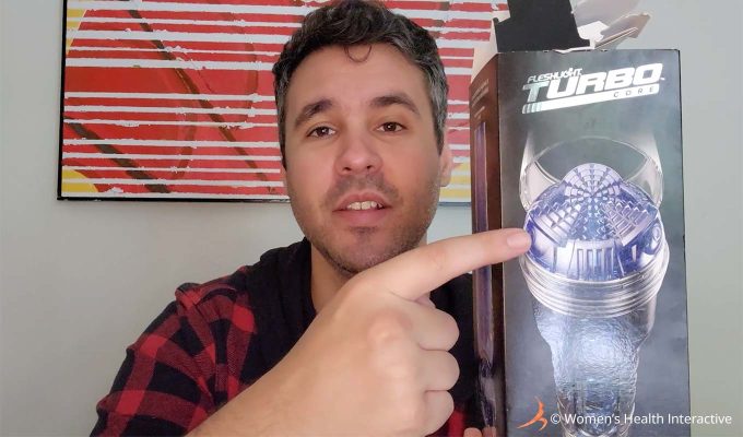 photograph of product tester justin holding the clear fleshlight turbo core box in his hand while pointing to the photograph of its mechanical looking orifice on the box