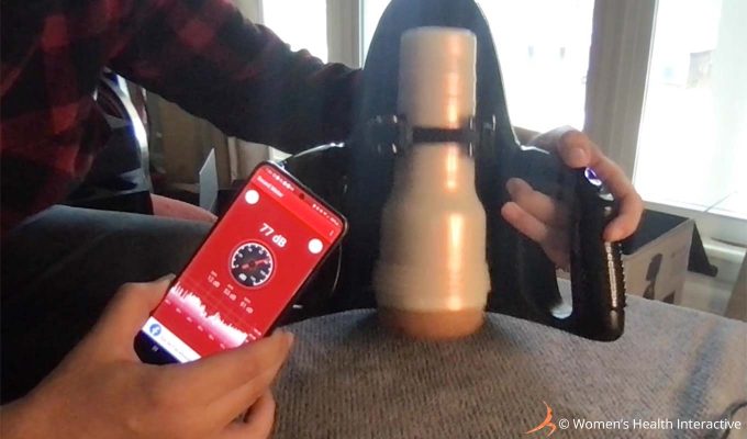 photograph of product tester justin performing decibel testing of the fleshlight universal launch automatic masturbator with a phone screen display reading 77 db