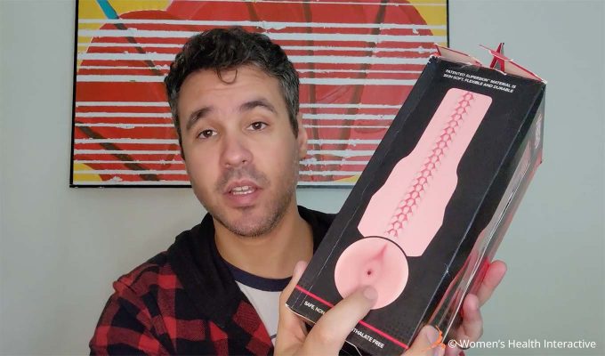 photograph of product tester justin holding the fleshlight vibro butt box in one hand while pointing to the orifice on the texture map printed on the back of the box