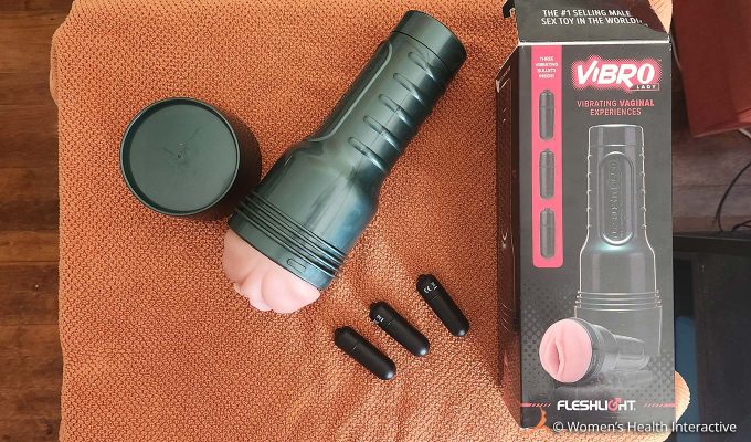 aerial photograph of the fleshlight vibro lady vibrating pocket pussy and stroker with its three bullet vibrators, cap, and box on a cloth surface