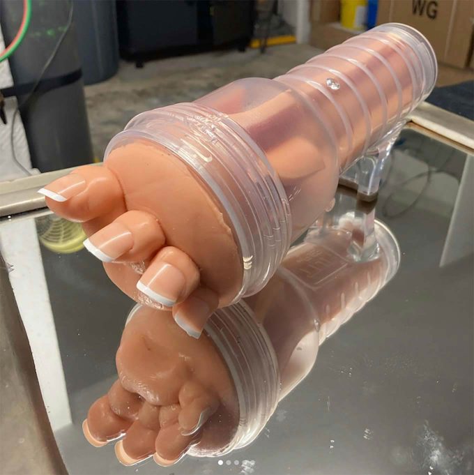 photograph of a foot-inspired fleshlight featuring four large toes with french manicured nails and a clear case designed to look like a glass slipper