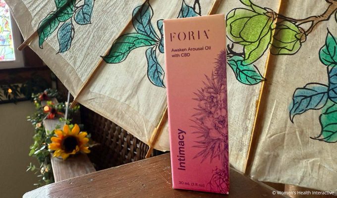 foria awaken arousal oil box on a wood post with a floral fan open behind it