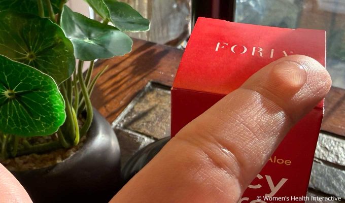 closeup detail of a single drop of foria juicy pure on the tip of a finger with the red foria box right beneath it