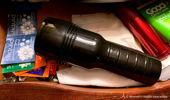 aerial photograph of a fleshlight with its cap on inside a nightstand drawer, which looks like an industrial flashlight amid other things in the drawer including packets of personal lubricant, a pencil sharpener, a small handkerchief, and other miscellaneous items