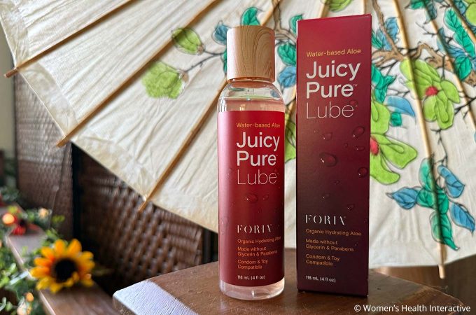foria juicy pure box and bottle on a small wood platform with a fan and flowers in the background