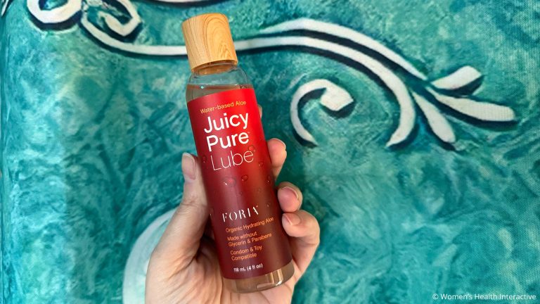 hand holding a bottle of foria juicy pure against a water-like blue painted background