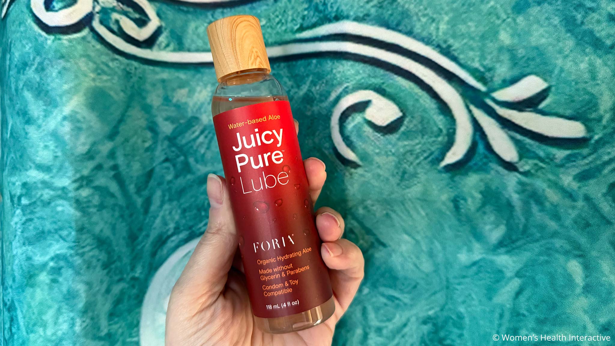 hand holding a bottle of foria juicy pure against a water-like blue painted background
