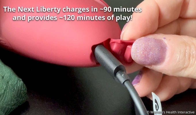 womanizer next liberty with charging cable plugged in and text stating that it charges in about 90 minutes for 120-minute play time