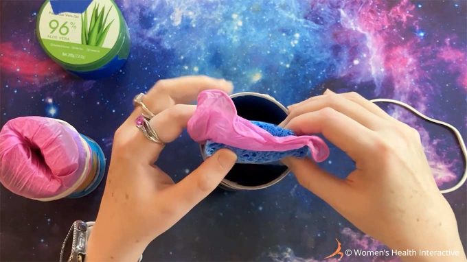 aerial photograph of hands inserting a glove sandwiched between two sponges into a pringles can