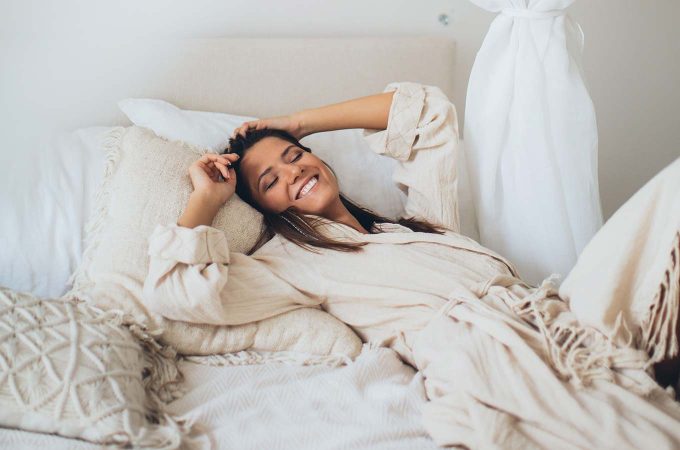 woman laying back in bed smiling
