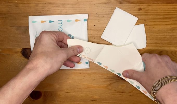 Photograph Of Julia's Hands Opening The Awkward Essentials Mainstream Over Wooden Tabletop