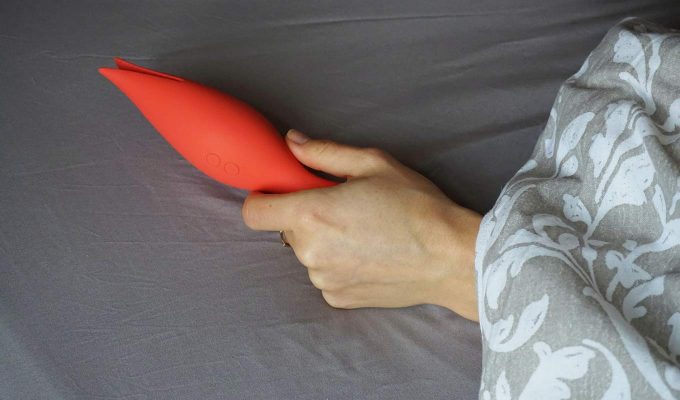 Photograph Of Flame-Shaped Vibrator Held In Hand Slipping Out From Beneath Heavy Blanket
