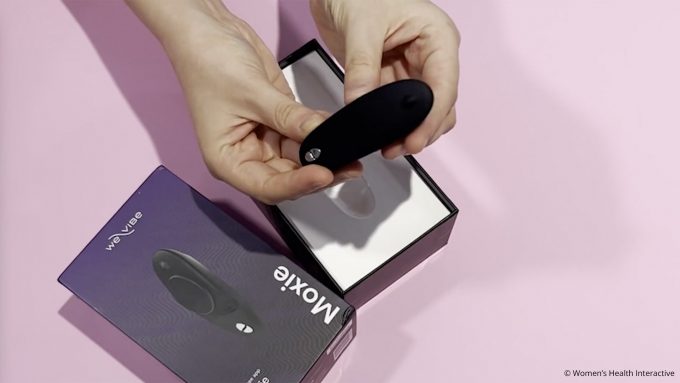 aerial photograph of hands holding we-vibe moxie panty vibrator over its open packaging, hands-on review concept