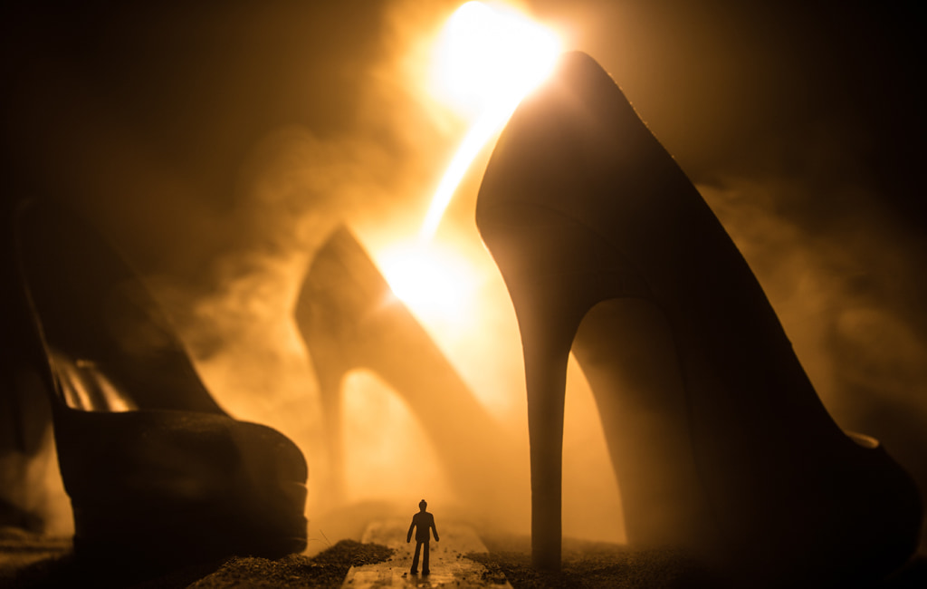 Surreal Concept, Silhouette Of Tiny Man Walking A Path Between Giant High Heel Shoes Against Smoky Golden Light