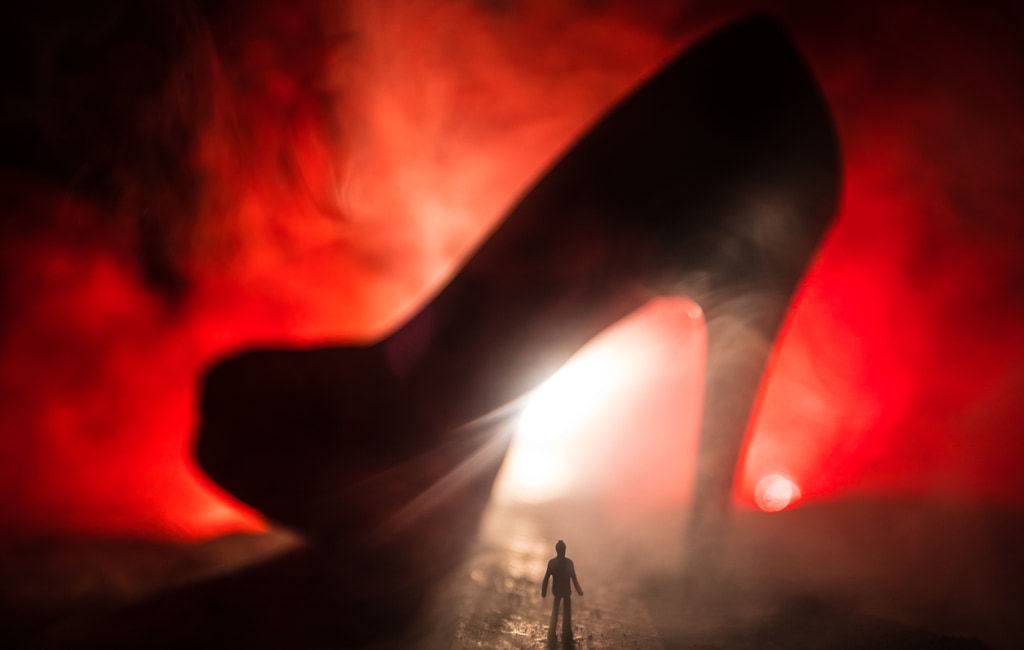 Surreal Concept, Silhouette Of Tiny Man Looking Up At A High Heel Shoe Against Deep Red Smoky Light