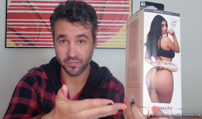 photograph of product tester justin holding the violet myers ahegao anal fleshlight in his hand while using his other hand to gesture toward it as though an invitation to the viewer to try it after reading his review of the anal pornstar fleshlight