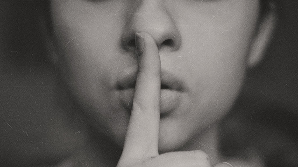 Close Up Of Woman's Face With Her Finger Over Her Lips As A Be Quiet Gesture