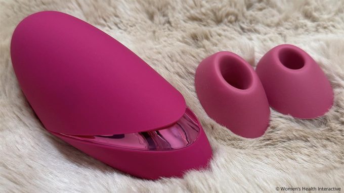 womanizer next liberty alongside its two mouth attachments and laying on a soft furry surface
